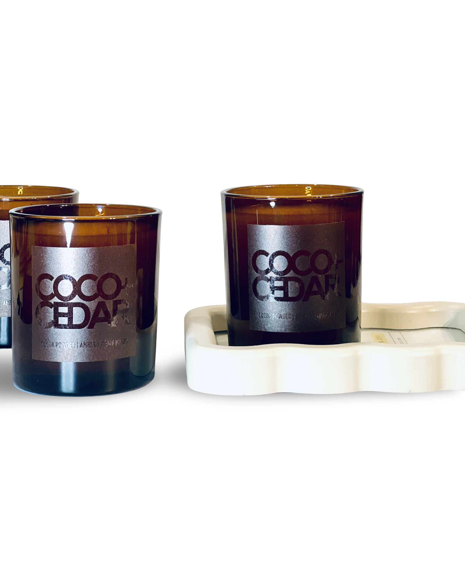 Three 'Coco Cedar' candles on a white surface with a white background